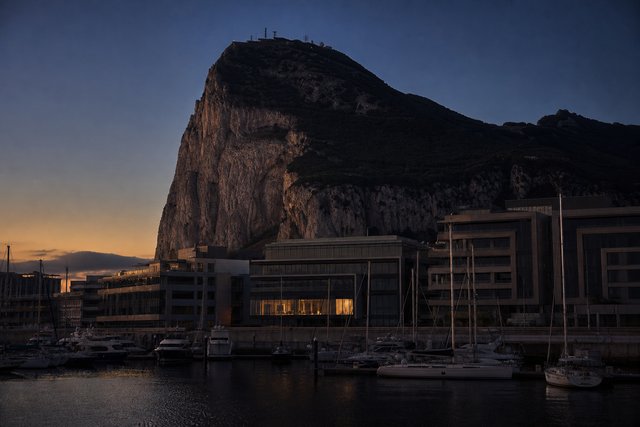 The Rock of Gibraltar rising behind low office blocks at dusk