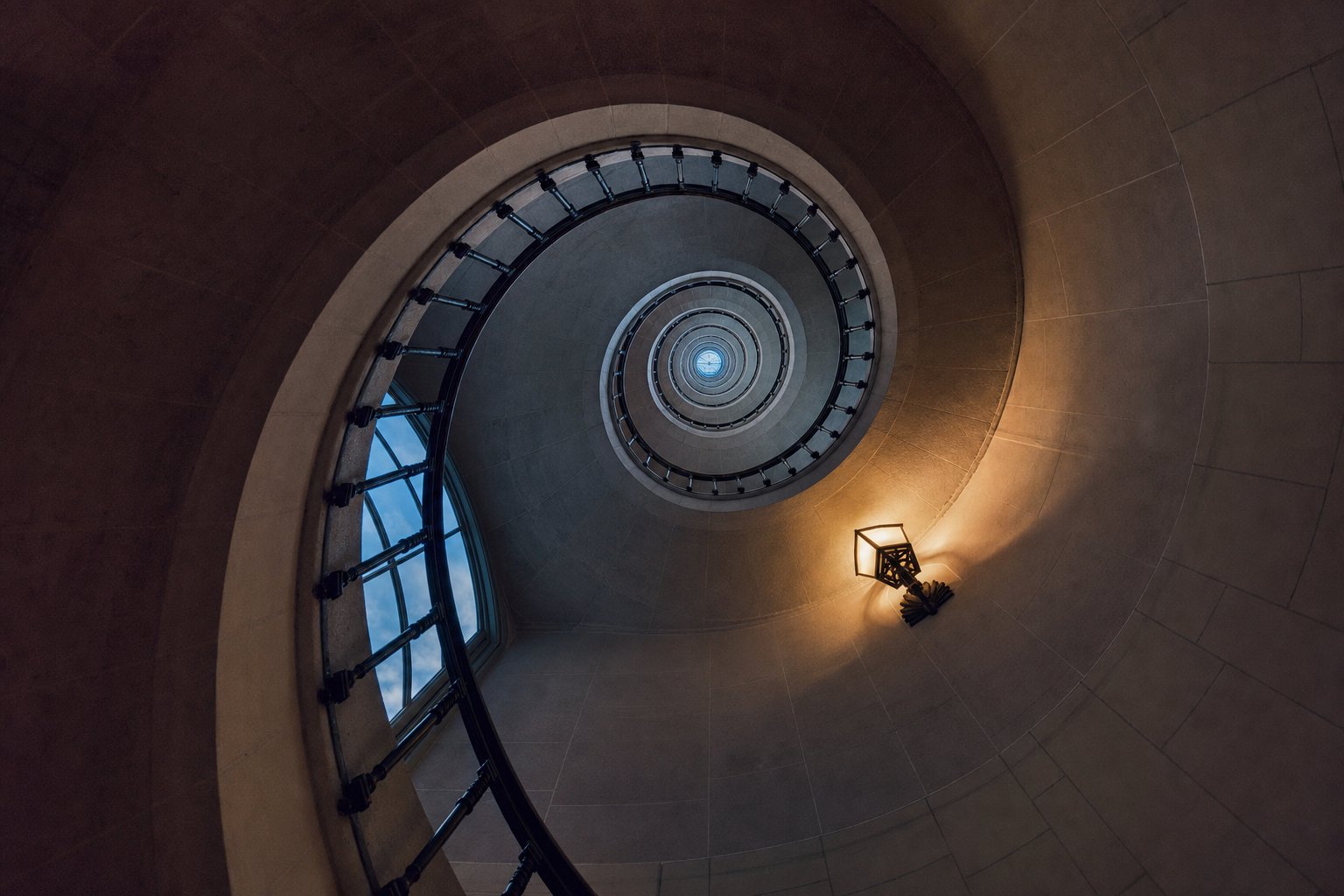 A stone spiral staircase photographed from directly below, its flights receding upward
